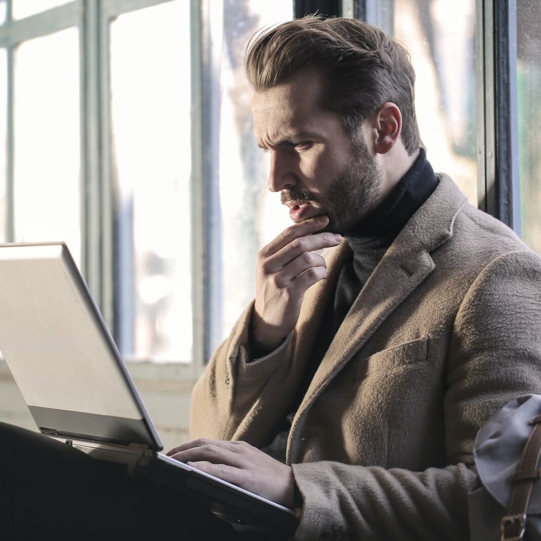 man holding his chin facing laptop computer